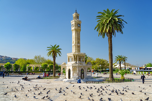 Izmir, Turkey - October 26, 2021: Scenic view of Izmir Clock Tower in the middle of Konak Square and a flock of pigeons. The tower is the landmark of the port city.