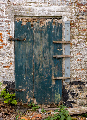 Abandoned house entrance with weathered wooden door and blathered paint.\nLocation: Flanders, Belgium