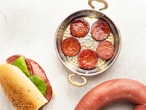 On a concrete table sits a small square black slate bearing a serving of roasted Nduja sausage.