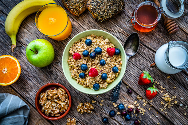 Healthy eating: overhead view of a green bowl filled with breakfast cereal, blueberries and raspberries. An orange juice glass, yogurt and some fruits and nuts are around the bowl. High resolution 42Mp studio digital capture taken with Sony A7rII and Sony FE 90mm f2.8 macro G OSS lens