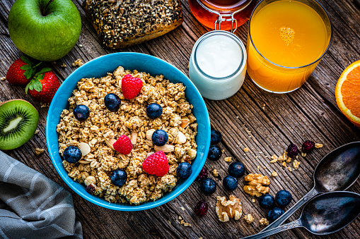 Healthy eating: overhead view of a blue bowl filled with breakfast cereal, blueberries and raspberries. An orange juice glass, yogurt and some fruits and nuts are around the bowl. High resolution 42Mp studio digital capture taken with Sony A7rII and Sony FE 90mm f2.8 macro G OSS lens