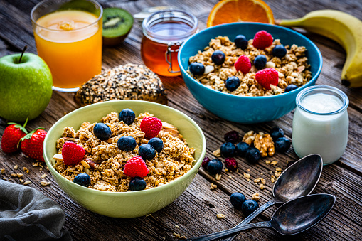 Healthy eating: two bowls filled with breakfast cereal, blueberries and raspberries. An orange juice glass, yogurt, honey jar and some fruits and nuts are around the bowl. High resolution 42Mp studio digital capture taken with Sony A7rII and Sony FE 90mm f2.8 macro G OSS lens
