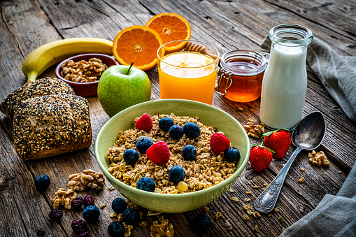 Healthy eating: high angle view of a green bowl filled with breakfast cereal, blueberries and raspberries. An orange juice glass, milk bottle and some fruits and nuts are around the bowl. High resolution 42Mp studio digital capture taken with Sony A7rII and Sony FE 90mm f2.8 macro G OSS lens