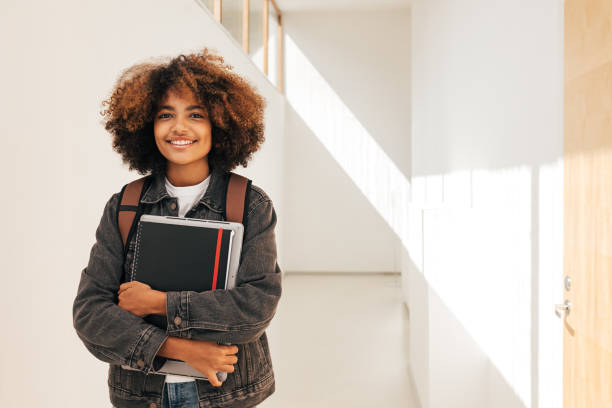 istock Portrait of a smiling student holding notebook and laptop while standing in corridor 1401338658