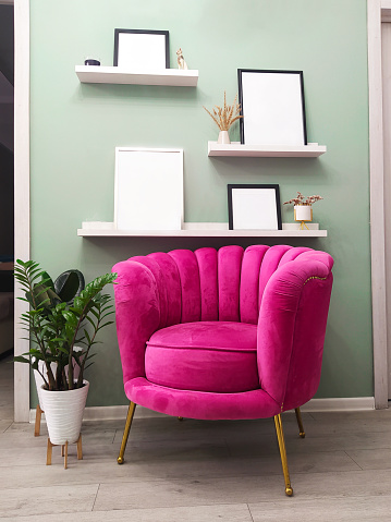 soft bright pink armchair in vintage style near the wall with photo frames, mockup, vintage style interiors