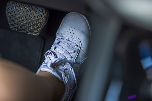 Close up view of female foot in white sneakers on electric vehicle gas pedal. Sweden.