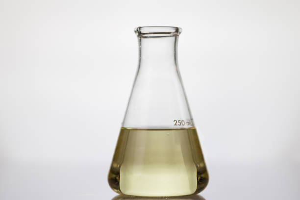 Yellow chemical liquid substance in a beaker with scientist in the background.