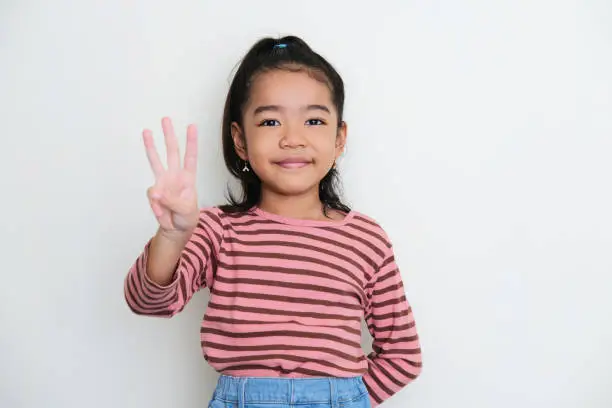 Photo of Asian little girl smiling to the camera and give three fingers sign