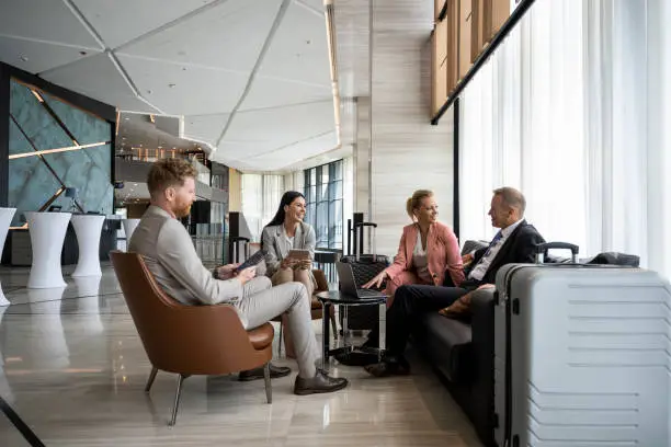 Photo of Four colleagues sitting in a luxury hotel lobby and preparing for a business meeting.