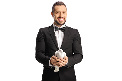 Smiling elegant young man in suit and bow-tie holding a white dove in his hands isolated on white background
