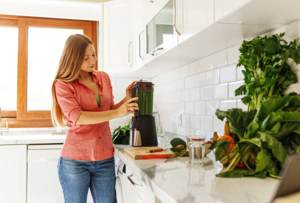 istock Cheerful young woman making smoothie using blender in the kitchen 1401341266