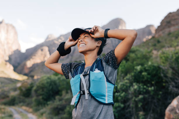 Happy woman in sportswear holding a cap looking at the mountains enjoying the hike stock photo