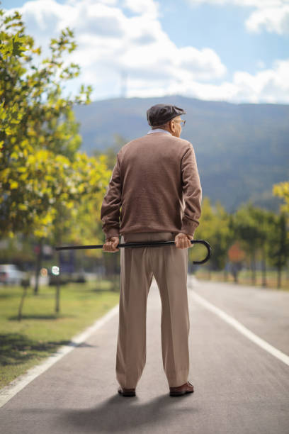 istock Elderly man standing and holding a cane behind his back outdoors 1401342143