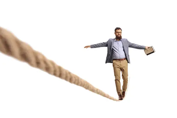 Full length portrait of a bearded young man holdind a book and walking on a tightrope isolated on white background