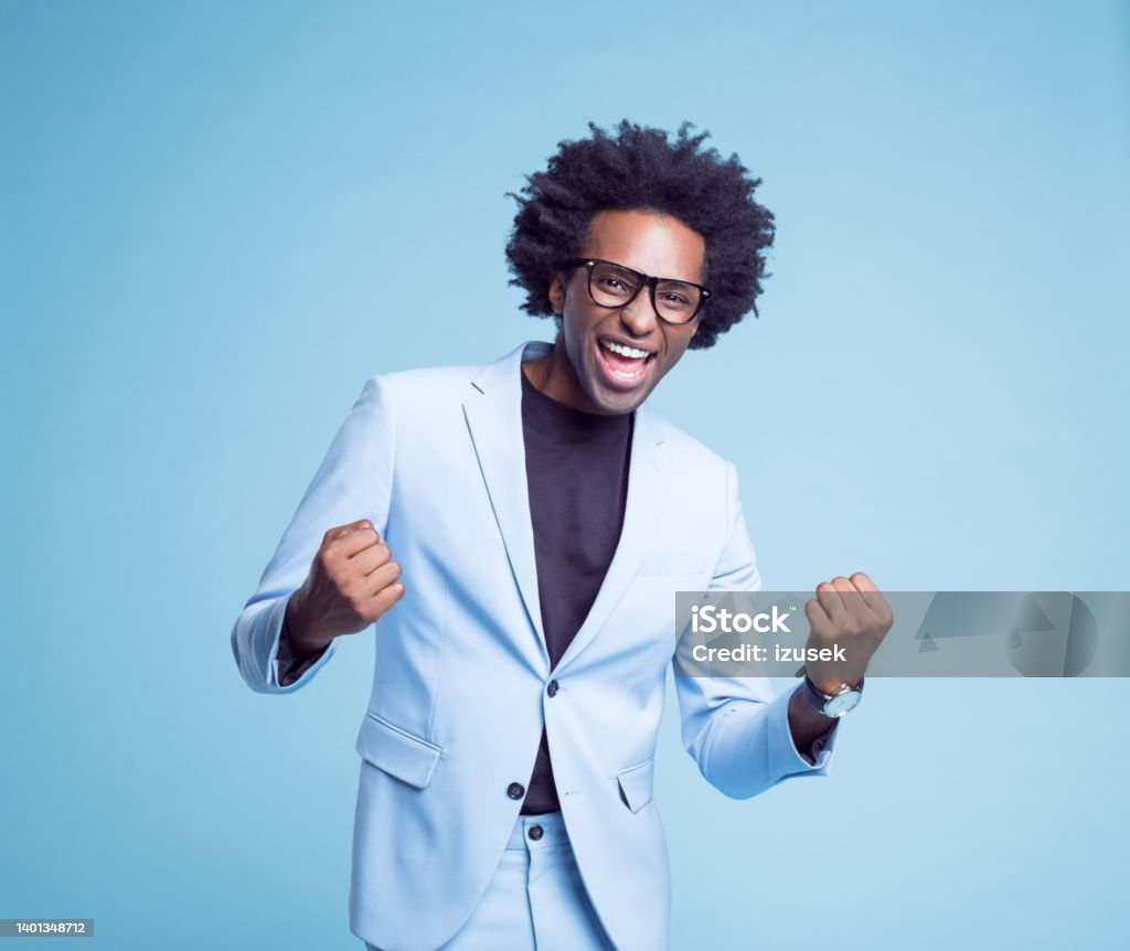 Happy businessman clenching fists Portrait of successful businessman with eyeglasses clenching fists against blue background Celebration Stock Photo