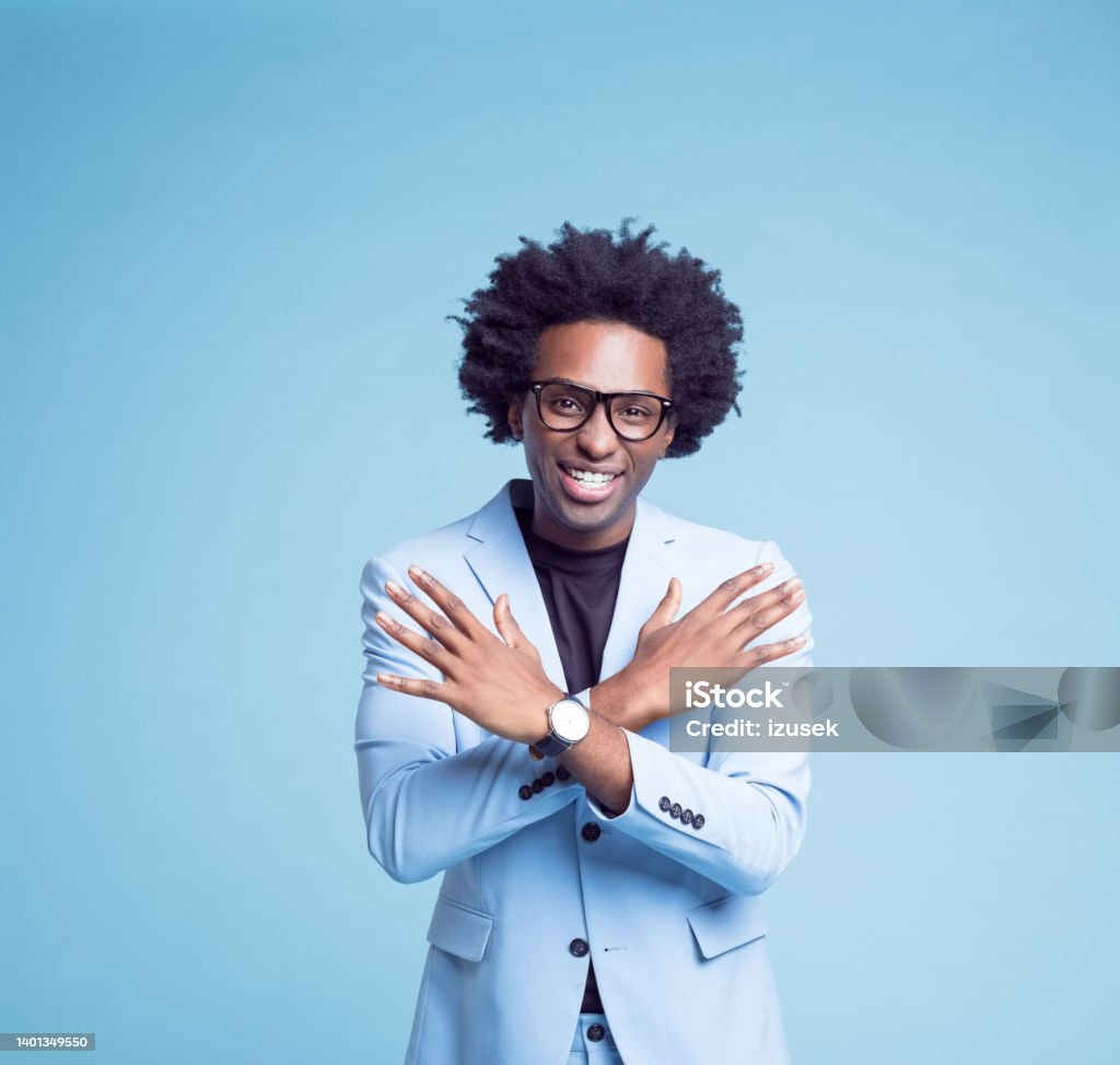 Smiling businessman showing cross gesture Portrait of happy businessman showing cross gesture against blue background. Sign Language Stock Photo