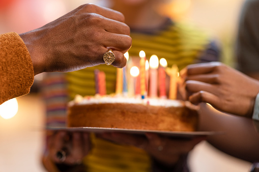 Close in shot of a hand lighting the candles on a birthday cake which is out of focus being held by somebody.