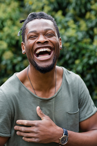 Young male adult belly laughing holding his stomach whilst standing outside and wearing casual clothing.