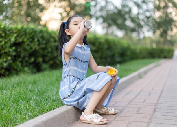Little girl sitting and drinking on the roadside
