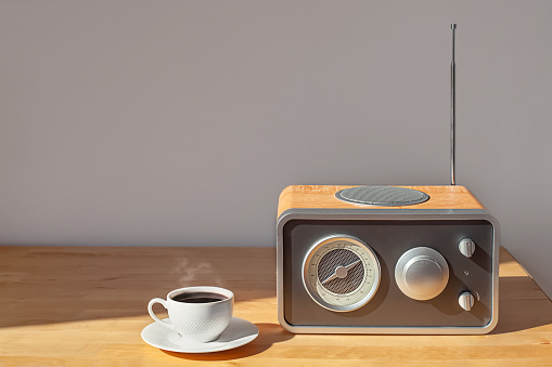 Un receptor de radio y una taza de café en una mesita de noche de madera bajo el sol de la mañana. photo