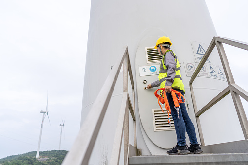 A female Asian maintenance engineer prepares to open the door of the wind turbine