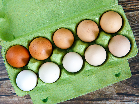 Colorful organic chicken eggs in green egg carton. These eggs were produced in small batches by a variety of chicken species so they appeared in different colors, patterns, and sizes. Top view
