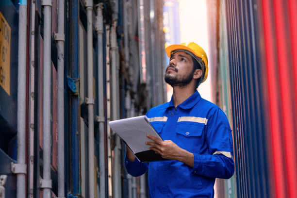 trabajador de control de muelle comprobando el embalaje completo del contenedor contra la pila de una terminal de contenedores. está trabajando en el patio de embarque mientras revisa el portapapeles. logística y transporte, conceptos de negocio global. - industrial ship dock worker engineer harbor fotografías e imágenes de stock