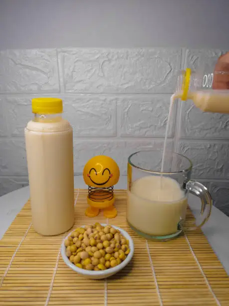 Bottle of Soymilk with soybean, and someone pouring Soymilk into glass