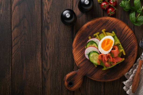 istock Savory waffles. Breakfast green waffles wild garlic or spinach with egg, tomato, salmon on wooden plate for breakfast on old dark wooden background. Light dinner, lunch or breakfast. Top view. Mock up 1401355543