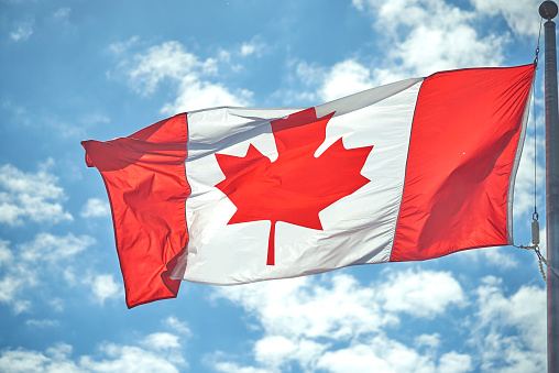 Happy Canada Day message next to tiny Canadian flag on blue  background. Horizontal composition with copy space. Front view.