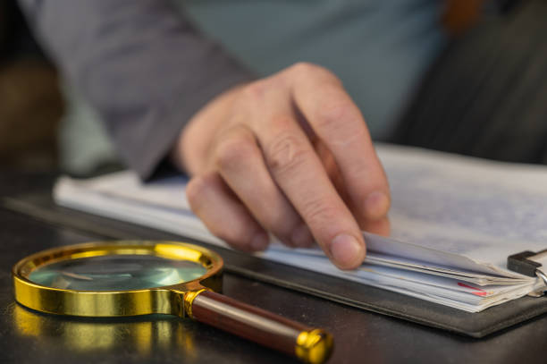 istock A man's hand is leafing through documents. Round magnifying glass with gold-colored frame in the foreground. A clipboard for papers. Inside the room. Selective focus. 1401360203