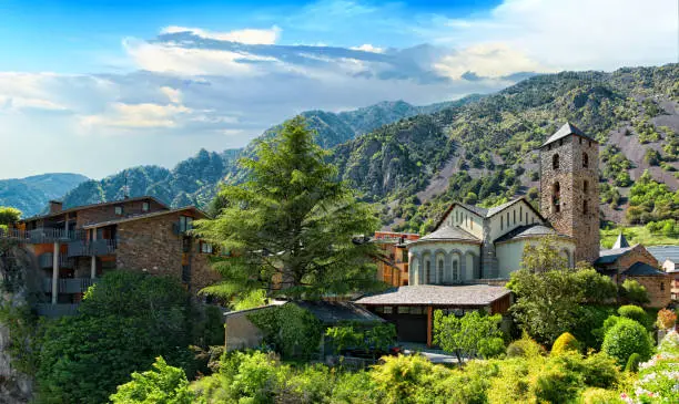 Scenic cityscape of Andorra la Vella city with old houses, ancient Church of Sant Esteve and mountain range against the blue sky on a sunny afternoon. Andorra la Vella, the capital of principality of Andorra