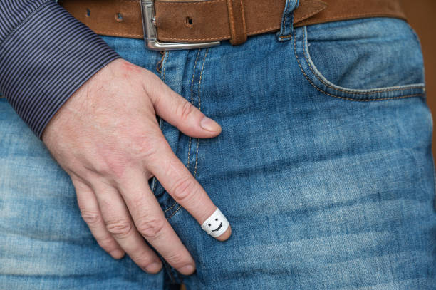 the man holds himself by the crotch with his hand. the man is middle-aged, caucasian. his index finger is wrapped in white tape. a happy smiling face is drawn in black marker on the finger. - 4609 imagens e fotografias de stock