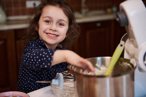 istock Cute European little assistant smiles cheerfully and makes funny faces while licking leftovers of whipped cheese cream in steel bowl at home kitchen 1401362688