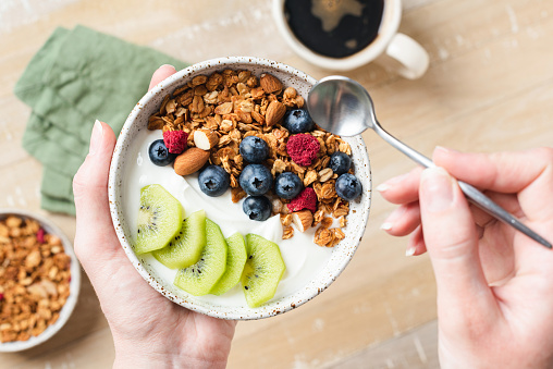 Female hands holding bowl of yogurt granola fruit bowl. Concept of clean eating, dieting, fitness food menu. Top view, selective focus