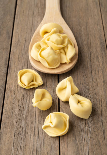 未調理のカッペレッティまたはトルテッリーニを木製のテ��ーブルの上にスプーンで置く - cappelletti ストックフォトと画像