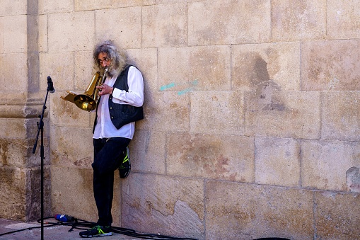 Barcelona, Spain - May 14, 2022. Musician leaning on a brick wall playing the flugelhorn, a wind instrument.