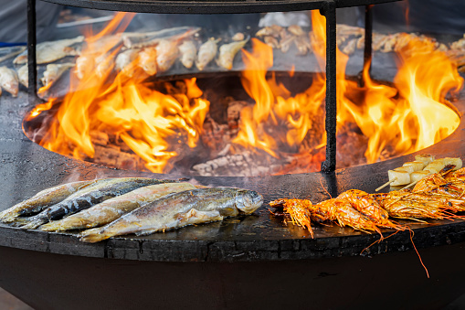 Fish, seafood prepared on barbecue grill outdoors close-up, fire flame in smoke, selective focus