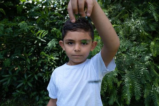 5 year old boy is brunette. Portrait point of view. Has a touching, sincere, emotional look. Back foliage. Child has white color on it.The child is pouring the leaves he has collected from the ground with his hand up. He is playing games with himself.