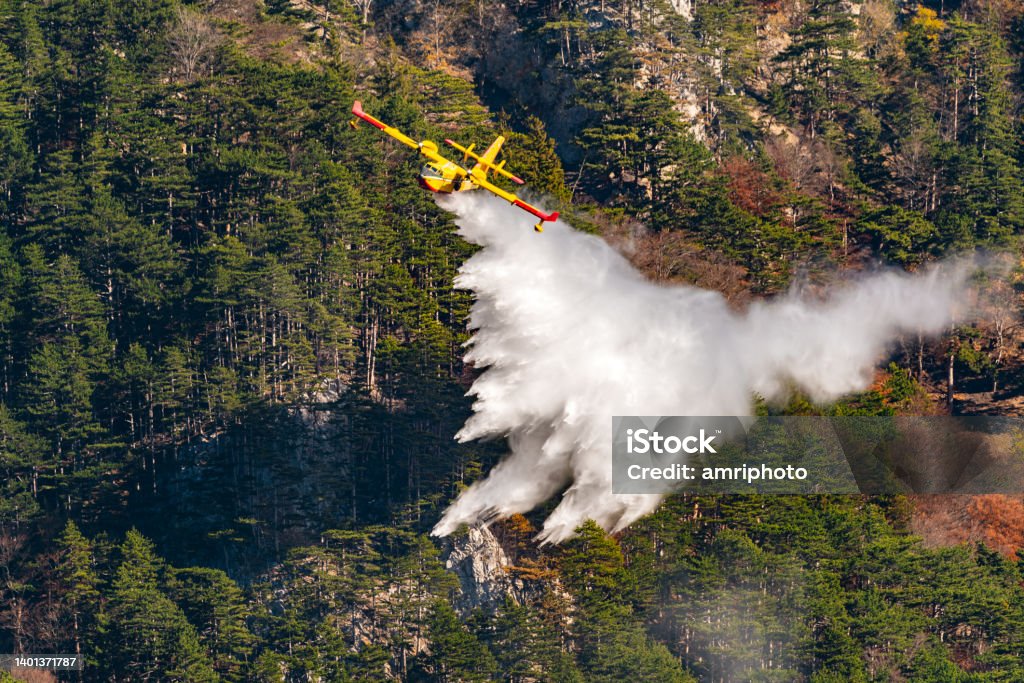 Firefighting aircraft dropping water over forest fire Firefighting aircraft extinguishing forest fire with lots of water in inaccessible area Forest Fire Stock Photo