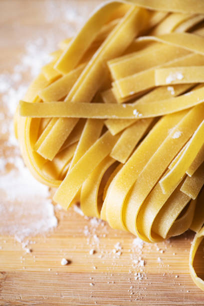 istock Fresh raw uncooked pasta - tagliatelle on a wooden board. 1401375837