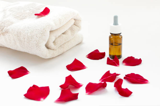 Aromatic oil, red rose petals and a towel on a light background