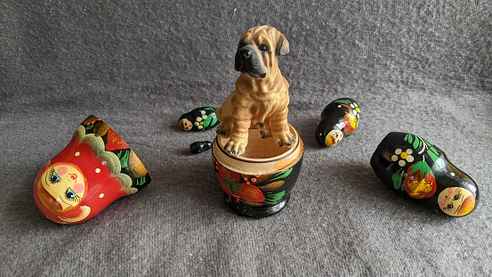 Front side A toy dog is placed on the bottom of an open matryoshka doll. Parts of a matryoshka doll on a gray background lie side by side.The idea of aggressive, deceptive and empty Russian culture.