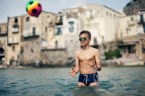 Teenage boy are playing with ball on beach. Vacations day in Cefalu, Sicily, Italy.\nShot with Canon R5