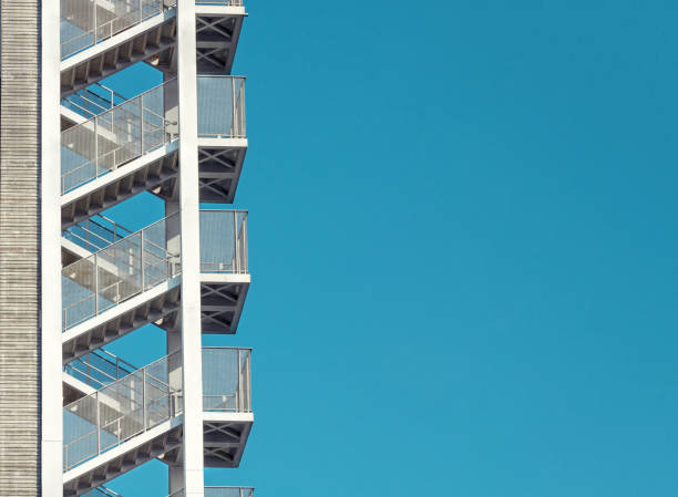 Close up, almost abstract, images of a partially constructed building featuring a metal framework and a staircase. The structure consists of girders and beams, suggesting it's in the early stages of construction, likely intended for multi-story use. The sky in the background is partly cloudy, providing natural lighting to the scene.