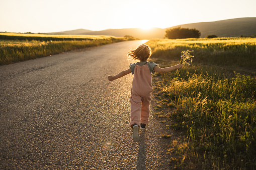 Little girl running on the street with flowers in her hand outdoors in sunset.