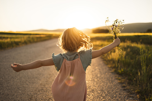 Little girl running on the street with flowers in her hand outdoors in sunset.