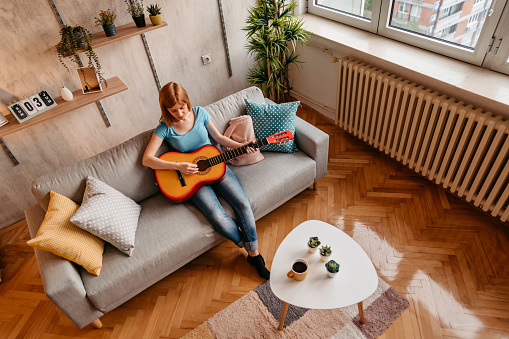 Young beautiful woman playing acoustic guitar on sofa at home.