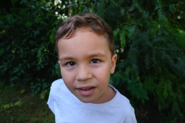 4 years old blond boy in white shirt.Portrait looking at camera.Having emotional expression.background is greenery