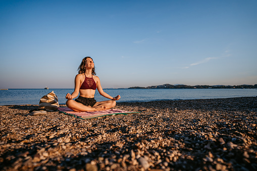 Beautiful young woman meditating and doing yoga on the beach.